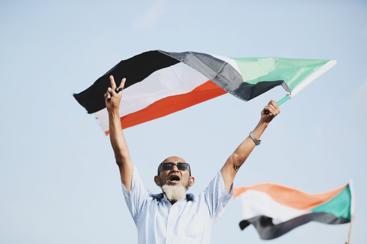 Man waves a Sudanese flag while holding up a peace sign with his fingers | Endure International December Prayer Guide