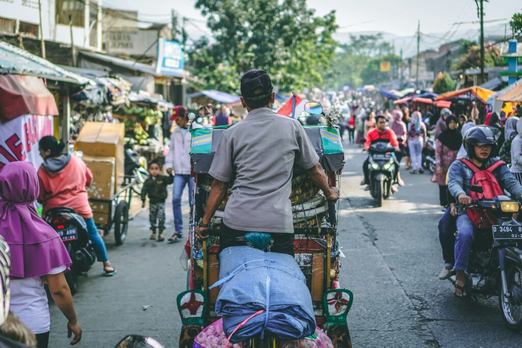 Man drives a rickshaw through a busy street in an Indonesian city