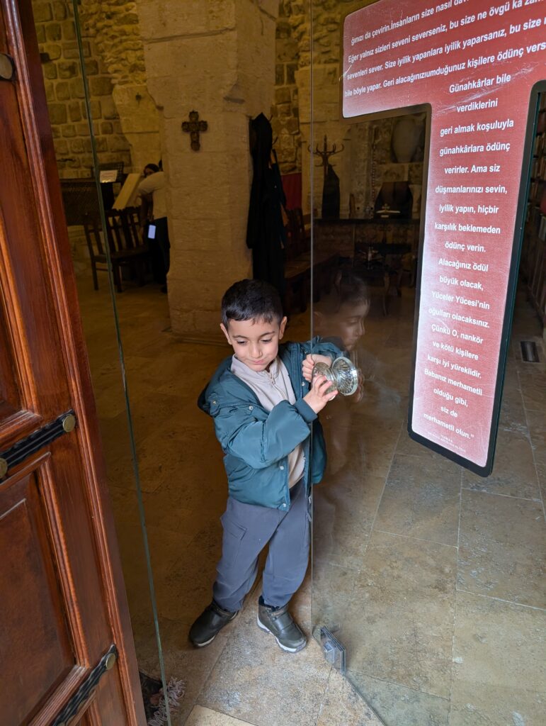 Small boy opens a tall glass door with a cross shaped sign on it leading into a historic monastery