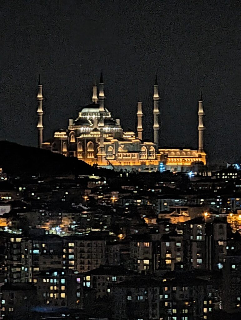 Large mosque brightly lit at night sits on a hilltop with a city below