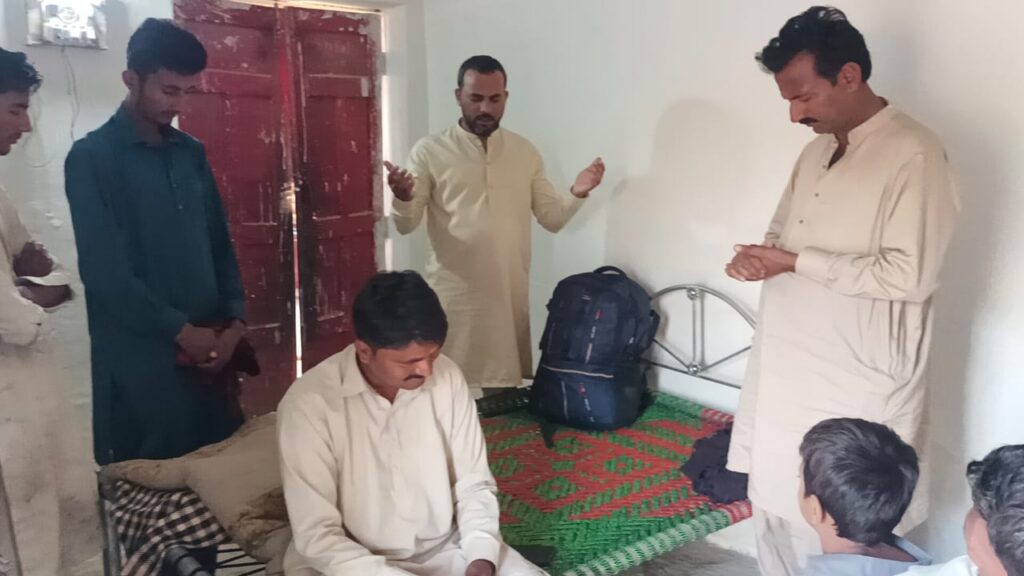 Five men stand and sit in a room together praying